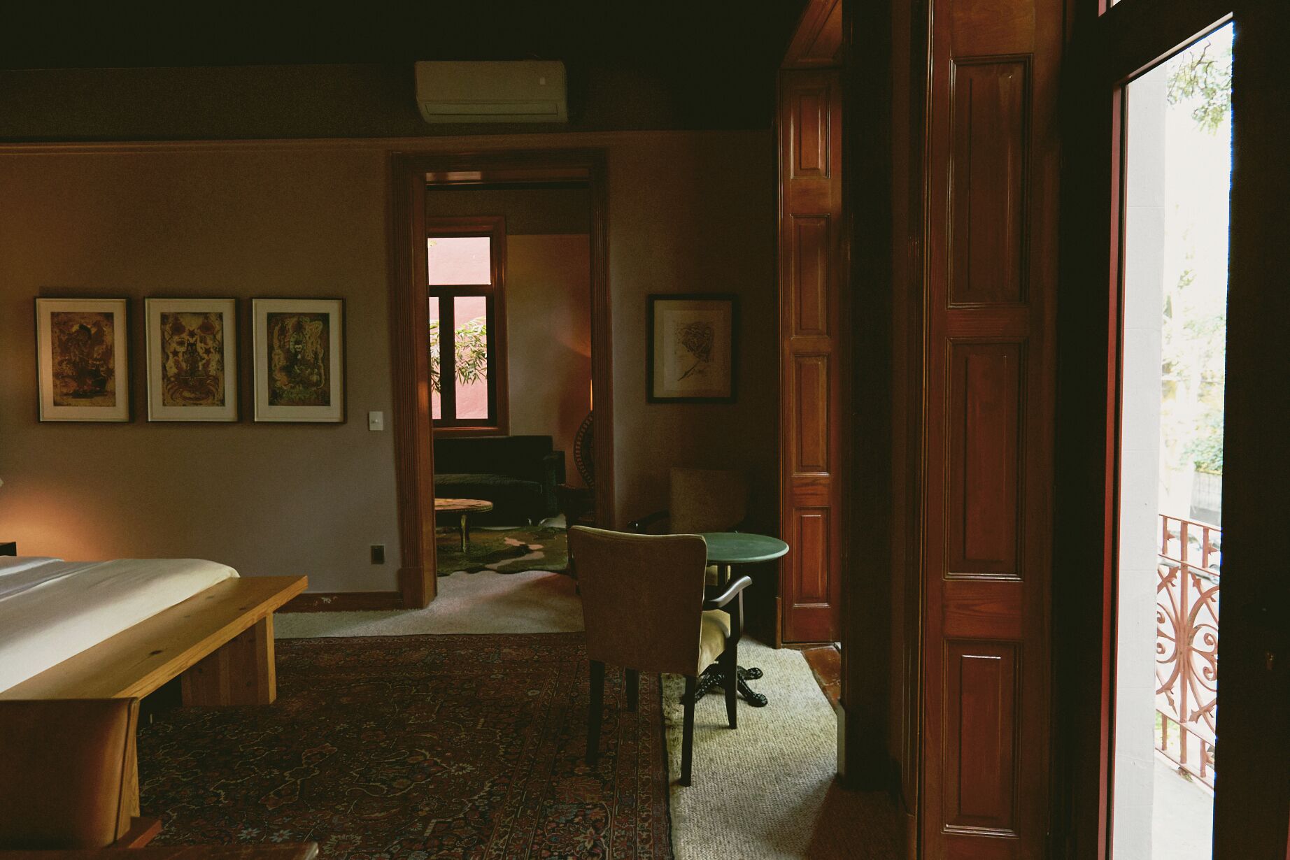 A room with a bed, a chair, a table, and a door leading to another room.
