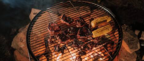 Un barbecue avec de la viande et du maïs, le tout disposé sur un lit de pierres.