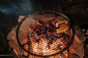Una parrilla con carne y mazorcas de maíz sobre una cama de piedras.