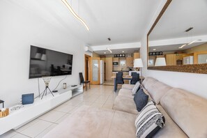 Ein modernes Wohnzimmer mit Flachbildfernseher, einer Couch, einem Essbereich und einer Küche im Hintergrund.