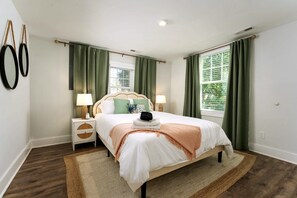 A bedroom with a bed, nightstands, lamps, a window with curtains, and a wall-mounted mirror. - Downtown Retreat - 5BR + Game Room - Pet Friendly (Wilmington)