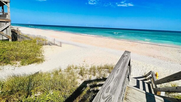 Ein Strand mit einer Holzpromenade, die zum Wasser führt, bewölkter Himmel und ruhige See.