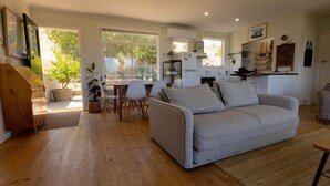 A modern living room with a grey sofa, wooden flooring, and a dining area with chairs and a table.