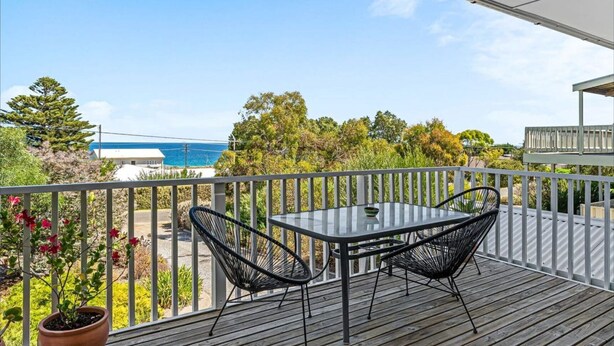 A balcony with a table and chairs, overlooking a residential area and a body of water.