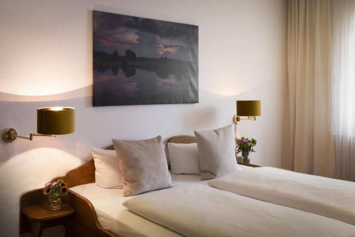 A hotel room with two beds, a painting on the wall, and two wall-mounted lamps.