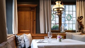 A dining area with a table set for two, a chandelier, and a view through a window with stained glass. - Romantik Landhotel 3Kronen (Adelsdorf)