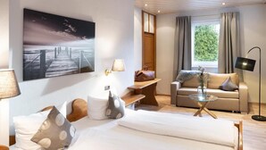 A modern hotel room with a bed, a sofa, a coffee table, and a large painting of a pier. - Romantik Landhotel 3Kronen (Adelsdorf)