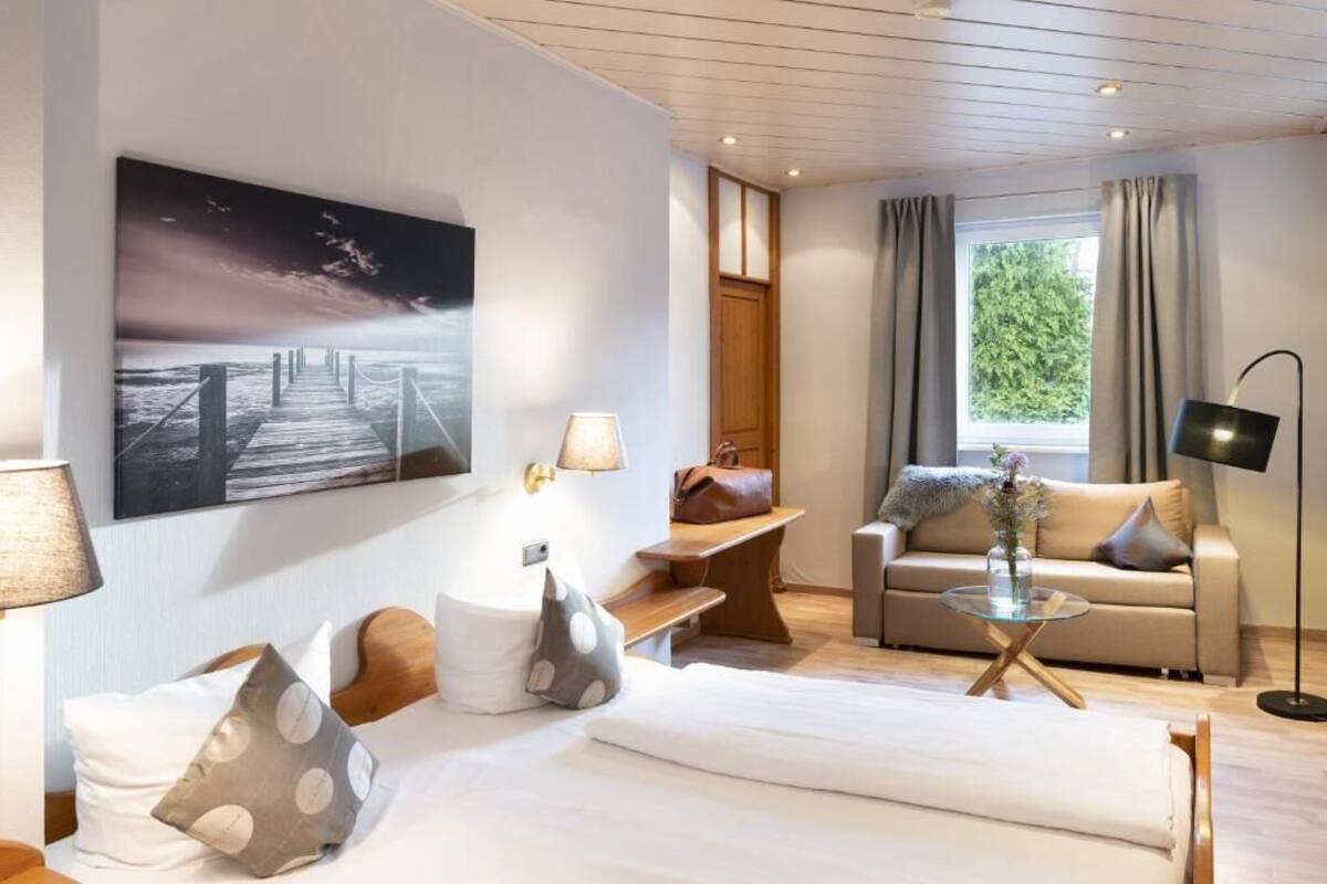 A modern hotel room with a bed, a sofa, a coffee table, and a large painting of a pier.