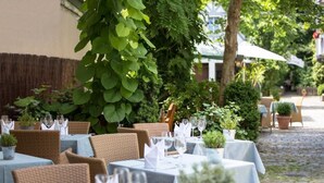 An outdoor dining area with wicker chairs and tables, surrounded by greenery and a cobblestone path. - Romantik Landhotel 3Kronen (Adelsdorf)