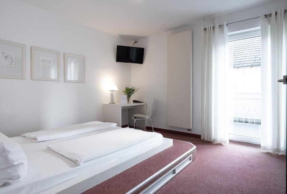 Een hotelkamer met een bed, een bureau, een stoel, een televisie en een raam met gordijnen.