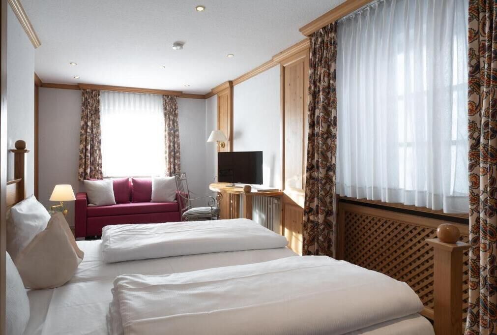 A hotel room with a bed, a TV, a sofa, and a window with curtains.