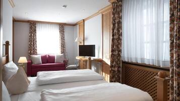 A hotel room with a bed, a TV, a sofa, and a window with curtains.