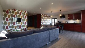 Ein modernes Wohnzimmer mit grauem Sofa, einem an der Wand montierten Flachbildfernseher und einer Küchenzeile mit roten Schränken.