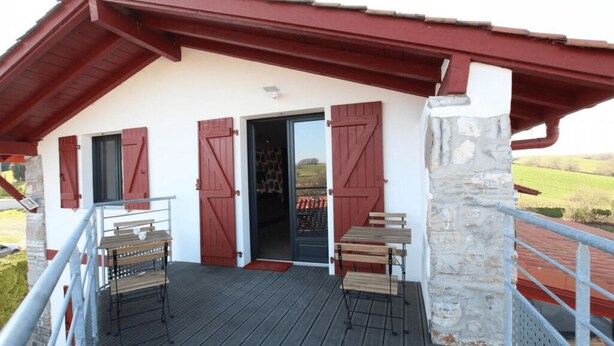 Ein Gebäude mit rotem Dach, einer Steinsäule und einer Holzterrasse mit zwei Tischen und Bänken.