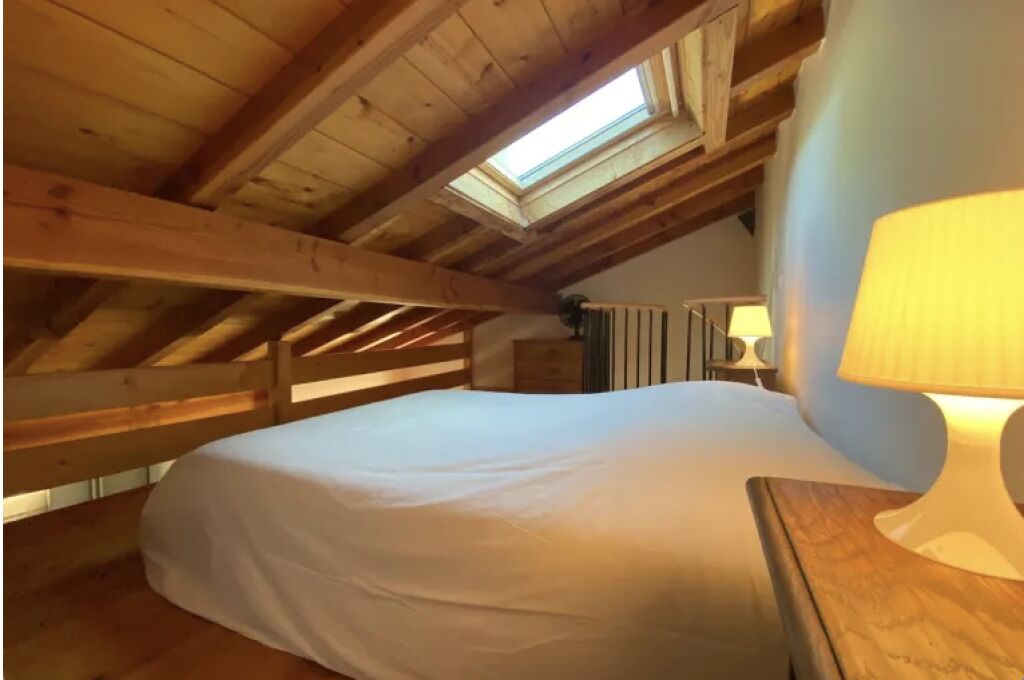 A bedroom with a skylight, a bed, a nightstand, and a lamp.