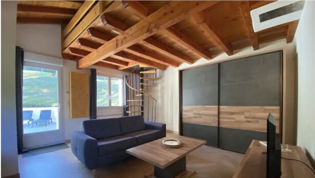 Een moderne woonkamer met een houten plafond, een bank, een salontafel, een televisie en een groot raam.