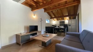 Een moderne woonkamer met een houten plafond, een flatscreentelevisie, een bank en een eethoek op de achtergrond.