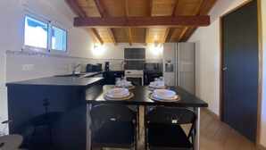 Een compacte keuken met een centraal eiland, een eethoek met stoelen en een houten plafond.