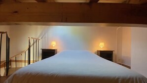 Een slaapkamer met een bed, twee bedlampen, een houten trap en een witte muur.