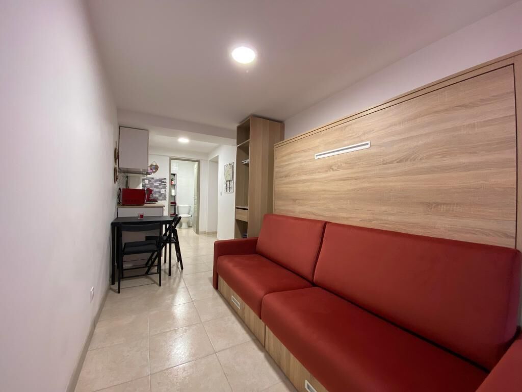 Un salon moderne avec un canapé rouge, un mur d’accent en bois et un coin cuisine à l’arrière-plan.