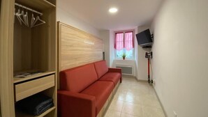 A room with a wooden wardrobe, a red sofa, a television mounted on the wall, and a window with pink curtains. - Aitzina Studio - Downtown (CAMBO LES BAINS)