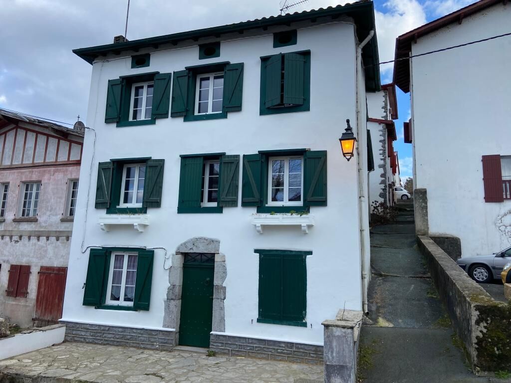 Un bâtiment blanc avec des volets verts et un escalier en pierre menant à une porte.