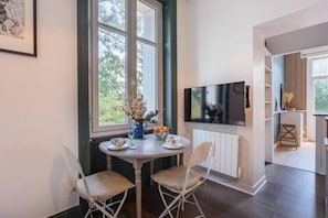 A room with a dining table, two chairs, a TV, and a window with a view of trees. - La Duchesse d'Anglet - Romantic studio (ANGLET)