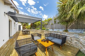 Una terraza de madera con mobiliario exterior, una pérgola y un muro de piedra.
