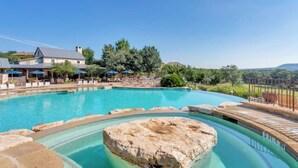 Ein Pool mit Felsen, Liegestühlen und einem Gebäude mit geneigtem Dach.