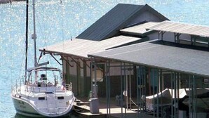 Ein Boot liegt in einer Marina vor Anker, mit einem überdachten Bauwerk, einer Bootsrampe und einem Gebäude mit geneigtem Dach.