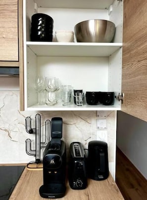 Une cuisine avec des meubles blancs, comprenant un appareil à café, un grille-pain et d’autres appareils électroménagers, ainsi qu’un dosseret en marbre.
