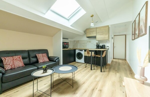 Un espace de vie compact comprenant un canapé, une table à manger, un lave-linge et un coin cuisine.