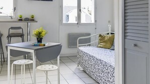 A room with a bed, a table with two chairs, a TV mounted on the wall, and a window with blinds.