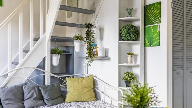 A bedroom with a bed, pillows, a hanging plant, and a staircase.