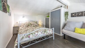 A bedroom with a bed, a grey wardrobe, a grey sofa, and a hanging plant.