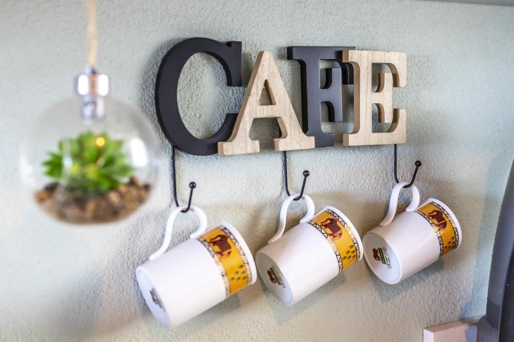 A wall with the word 'CAFE' in large letters, three mugs hanging below, and a hanging light fixture.