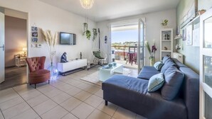 A modern living room with a sofa, armchair, TV, and balcony with outdoor furniture. - Le Lodge de Boucau - T2 with Balcony (BOUCAU)