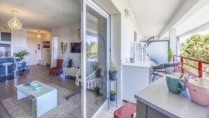A modern living space with a glass sliding door leading to a balcony, a kitchen area, and a seating area with a table and chairs. - Le Lodge de Boucau - T2 with Balcony (BOUCAU)