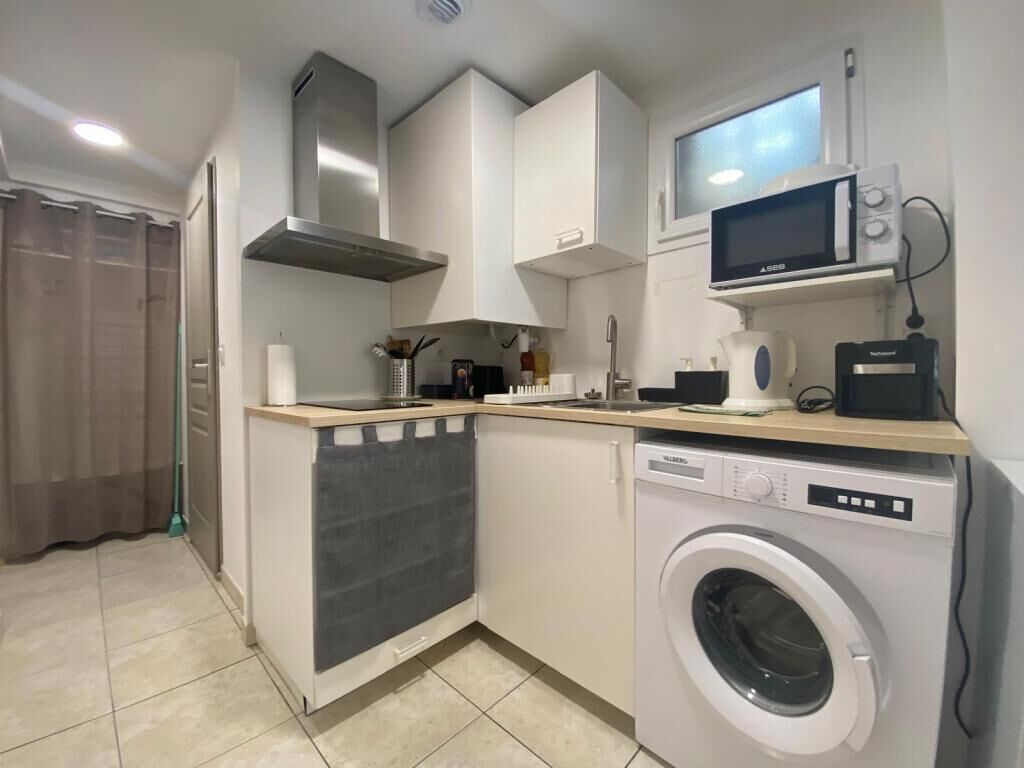 A compact kitchen with a washing machine, microwave, and a small countertop with various appliances.