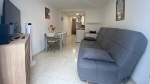 Ein modernes Wohnzimmer mit grauem Sofa, einem Holztisch, einem weißen Esstisch und einer Küche im Hintergrund.