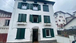 Ein zweistöckiges Gebäude mit grünen Fensterläden, einem gepflasterten Innenhof und einem gut erkennbaren Eingang.