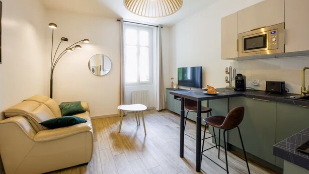 Un espace de vie compact comprenant un canapé, une petite table à manger, un téléviseur, un four à micro-ondes et un coin bar.