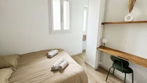 Une chambre à coucher avec un lit, deux serviettes enroulées, une chaise, une étagère avec un vase et une fenêtre.