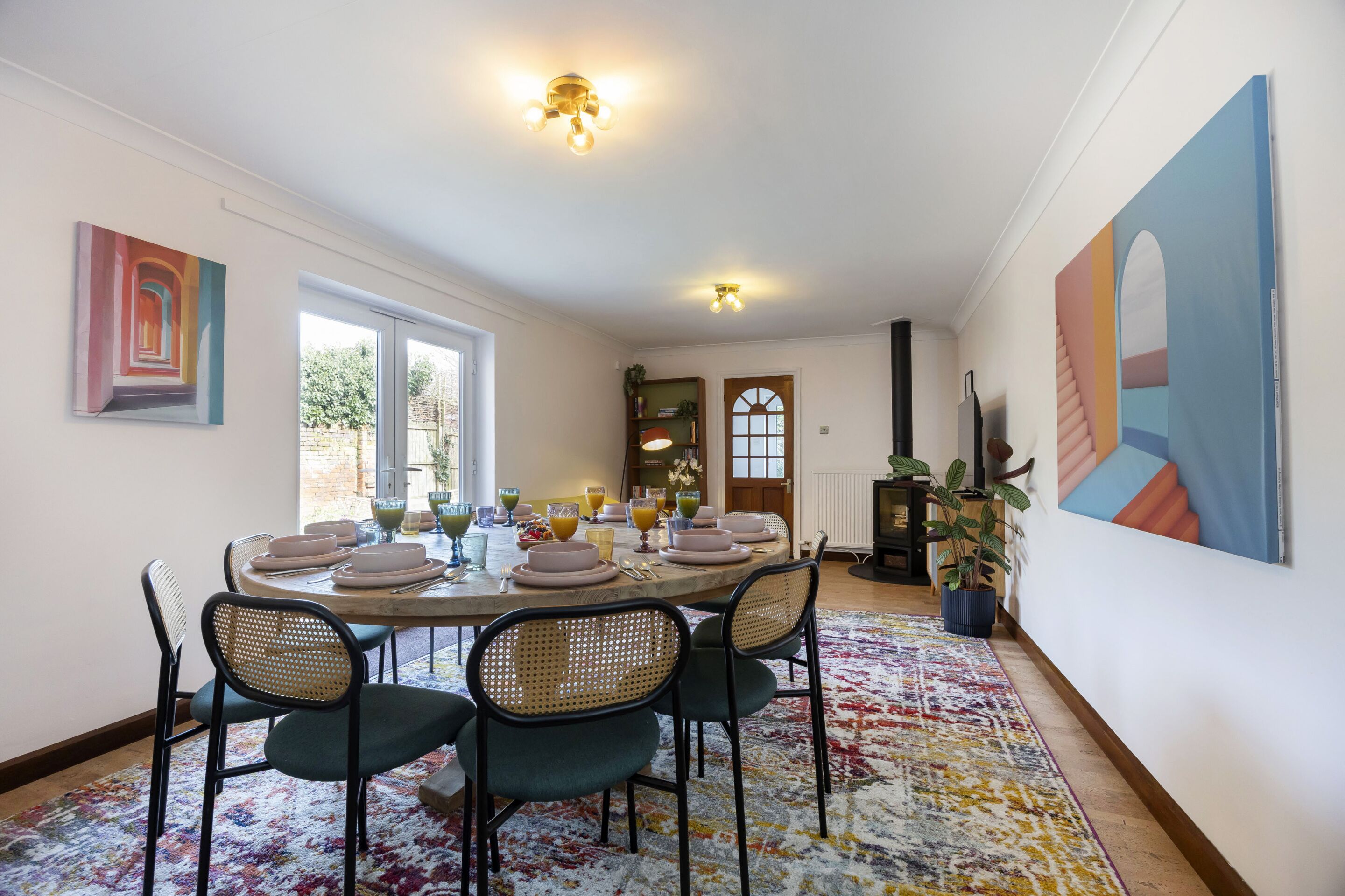 Un coin repas avec une table ronde dressée pour quatre personnes, entourée de chaises en osier, d’un tapis à motifs et d’œuvres d’art accrochées aux murs.