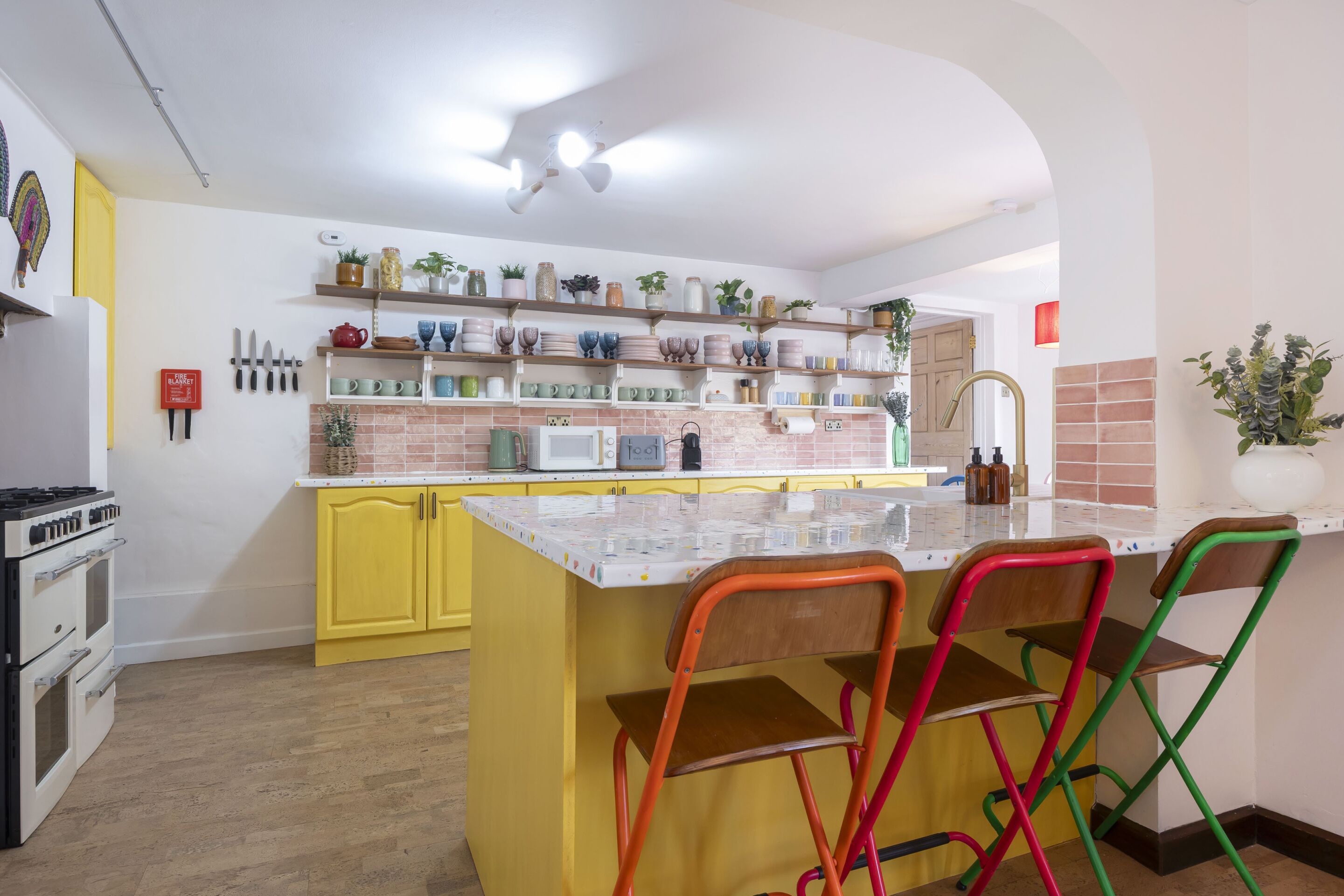 Une cuisine avec des meubles de couleur jaune, un îlot central et des chaises aux couleurs vives.