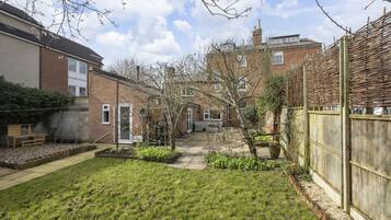 A residential backyard with a lawn, a wooden bench, a brick wall, and a garden bed.