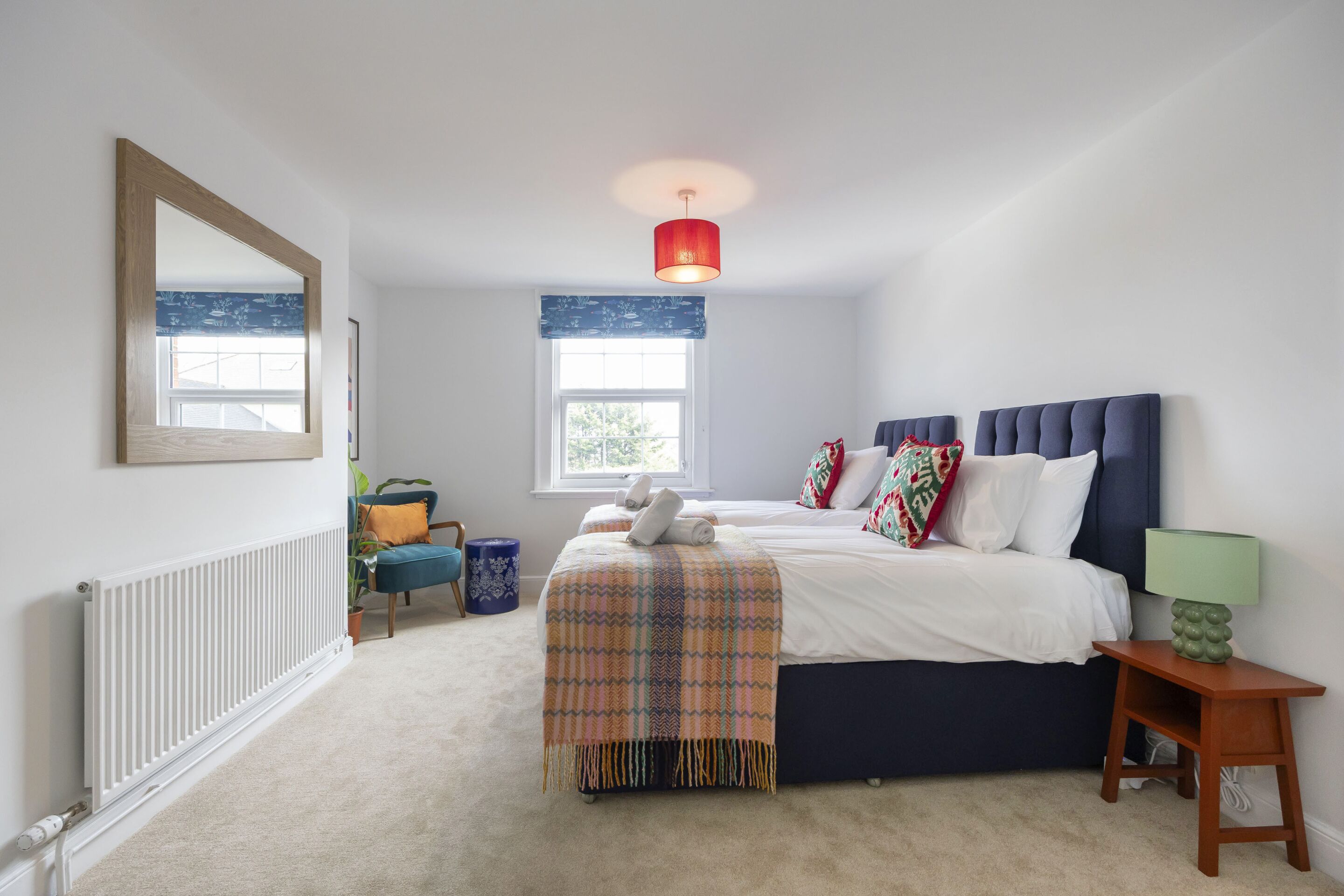 A bedroom with a bed, a bedside table, a lamp, a window, a radiator, and a mirror.