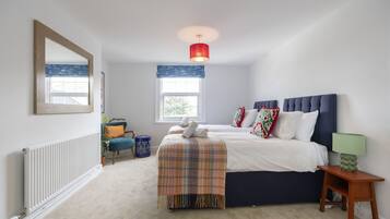 A bedroom with a bed, a bedside table, a lamp, a window, a radiator, and a mirror.