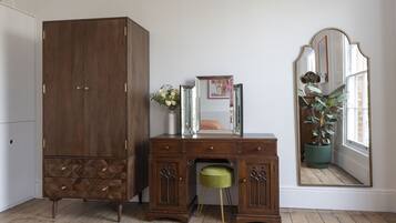 A room with a wooden wardrobe, a desk with drawers, a mirror, and a potted plant.