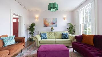 A living room with a green pendant light, a beige sofa with blue pillows, a purple sofa, and a pink ottoman.